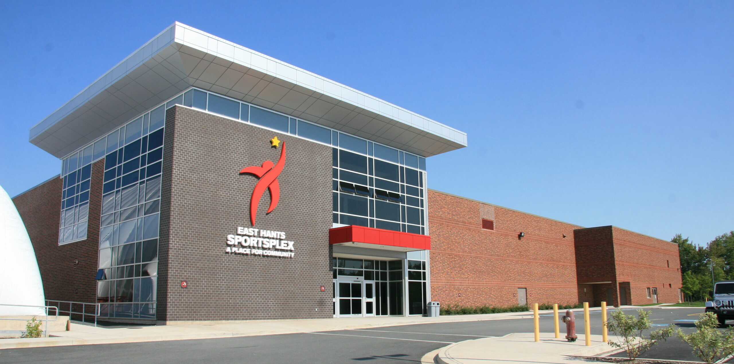 A two-storey grey brick atrium addition to an existing red brick arena.