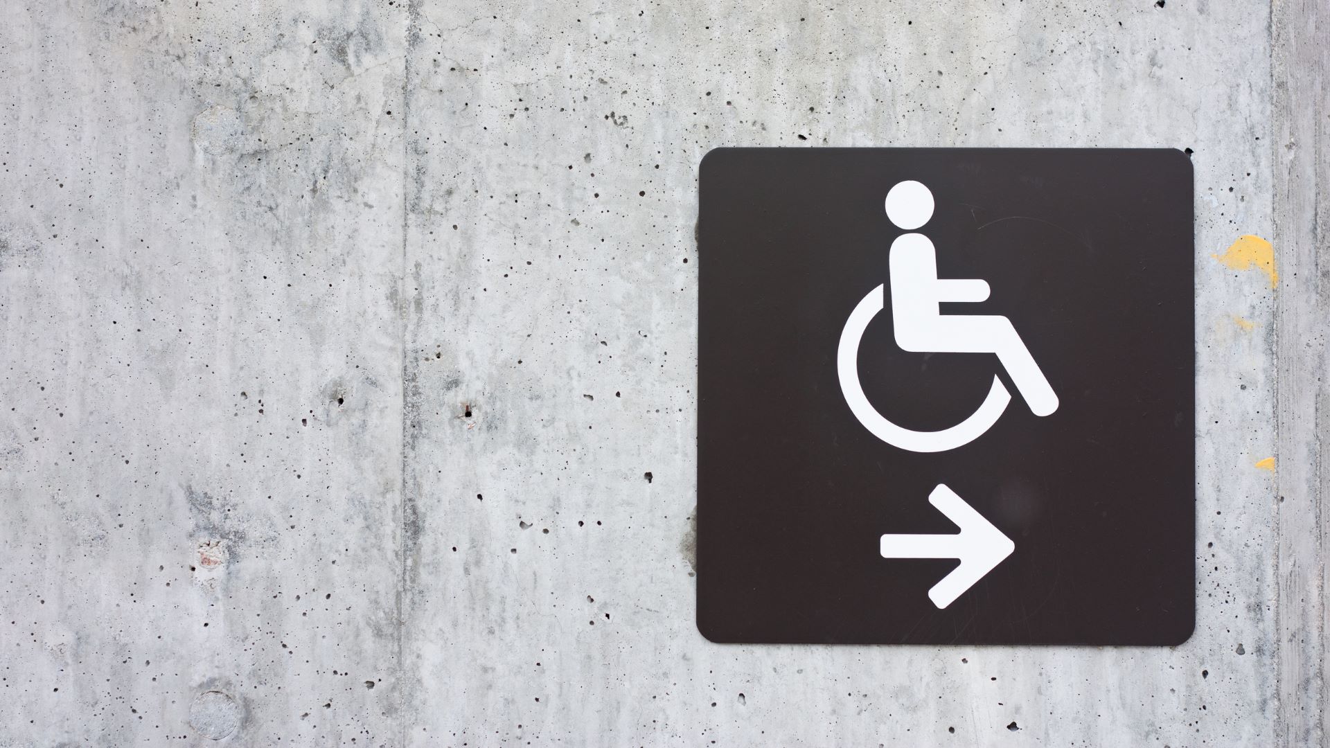 A black and white accessibility sign on a concrete wall