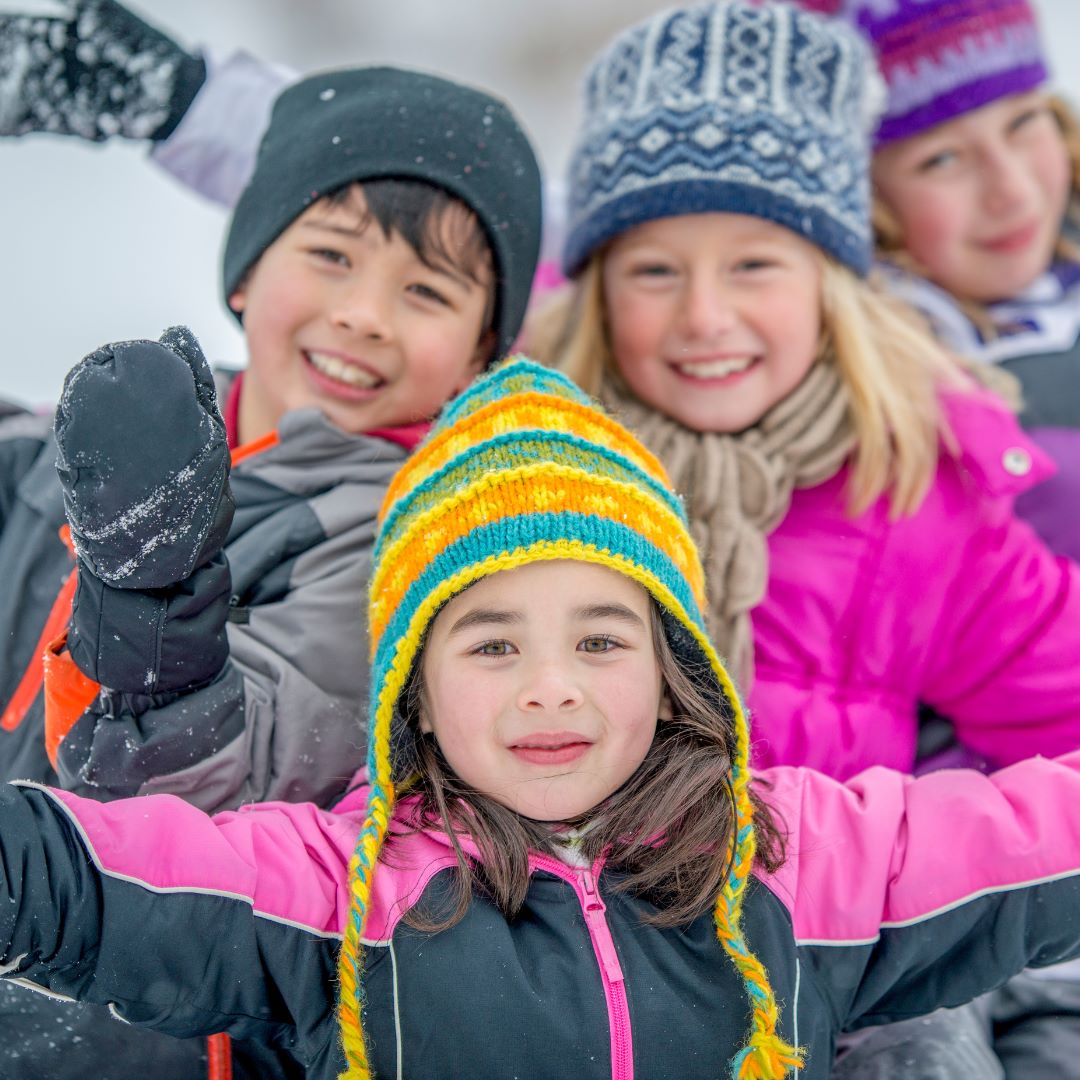 Children dressed in snow gear smiling with their arms held up