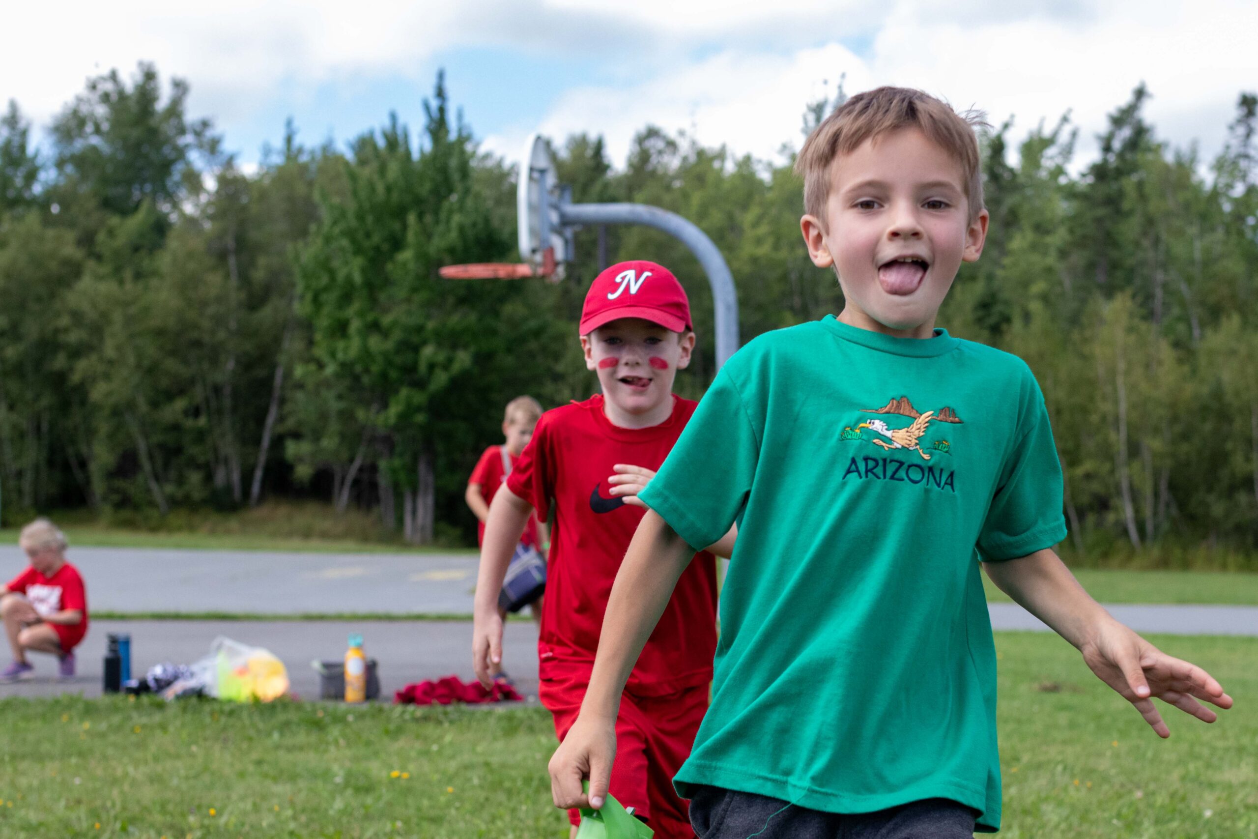 two young boys at a park run towards the camera with their tongues out
