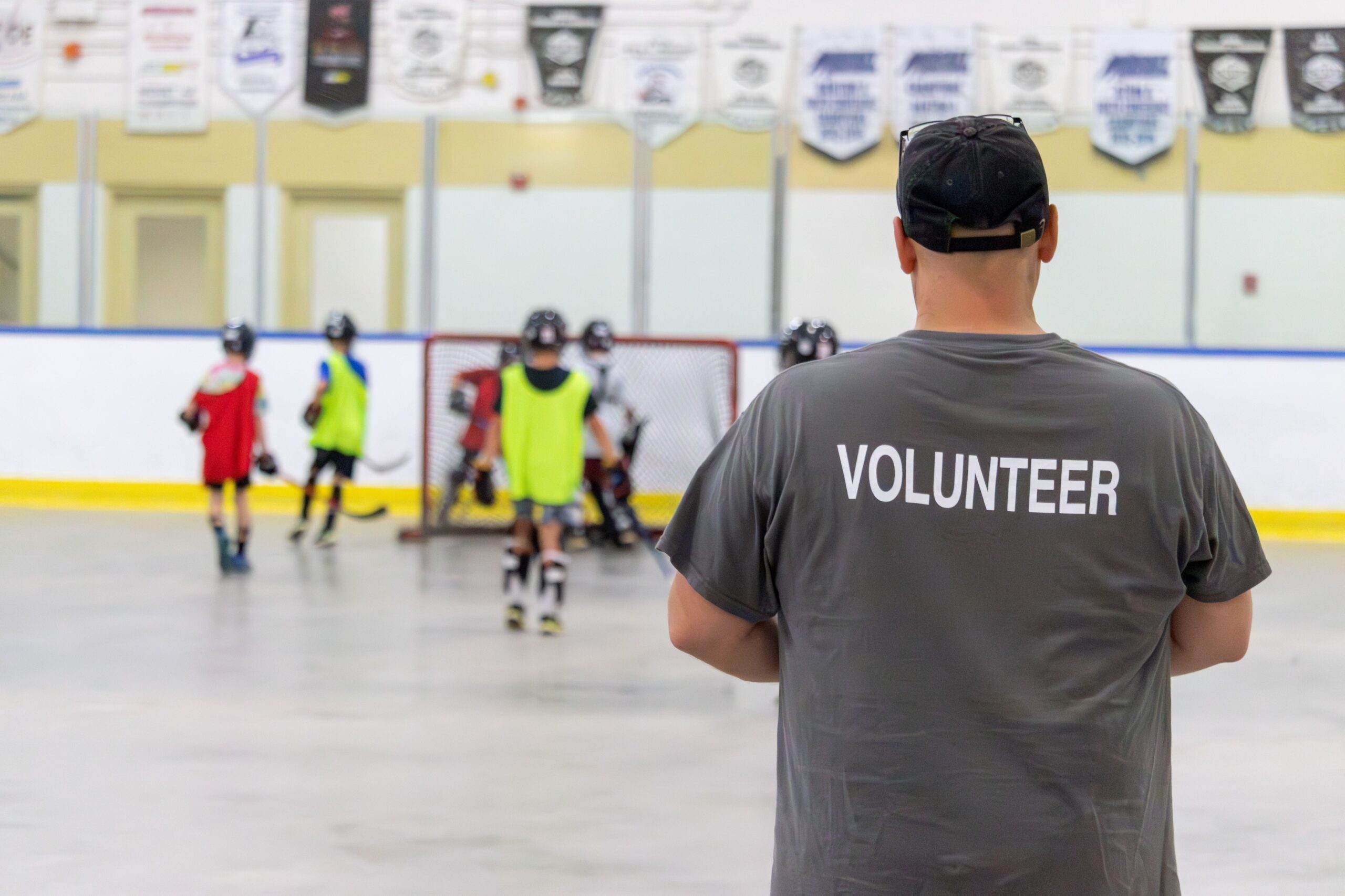 Man with his back to the camera wearing a volunteer shirt watches ball hockey