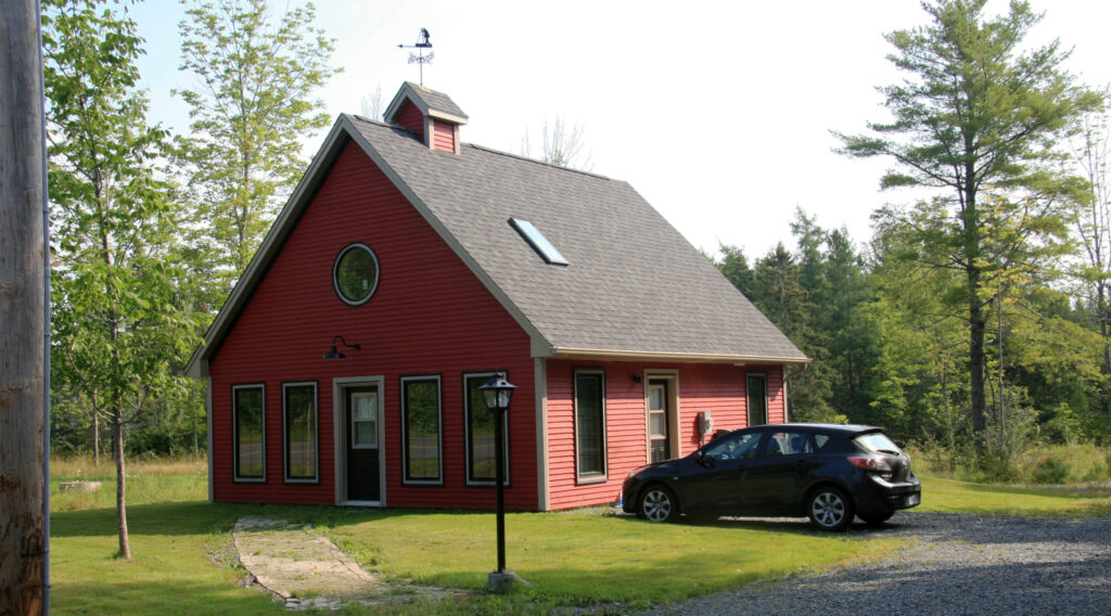 A red-sided home with a steep pitched roof, circular window, and small belfry with a weather vane.