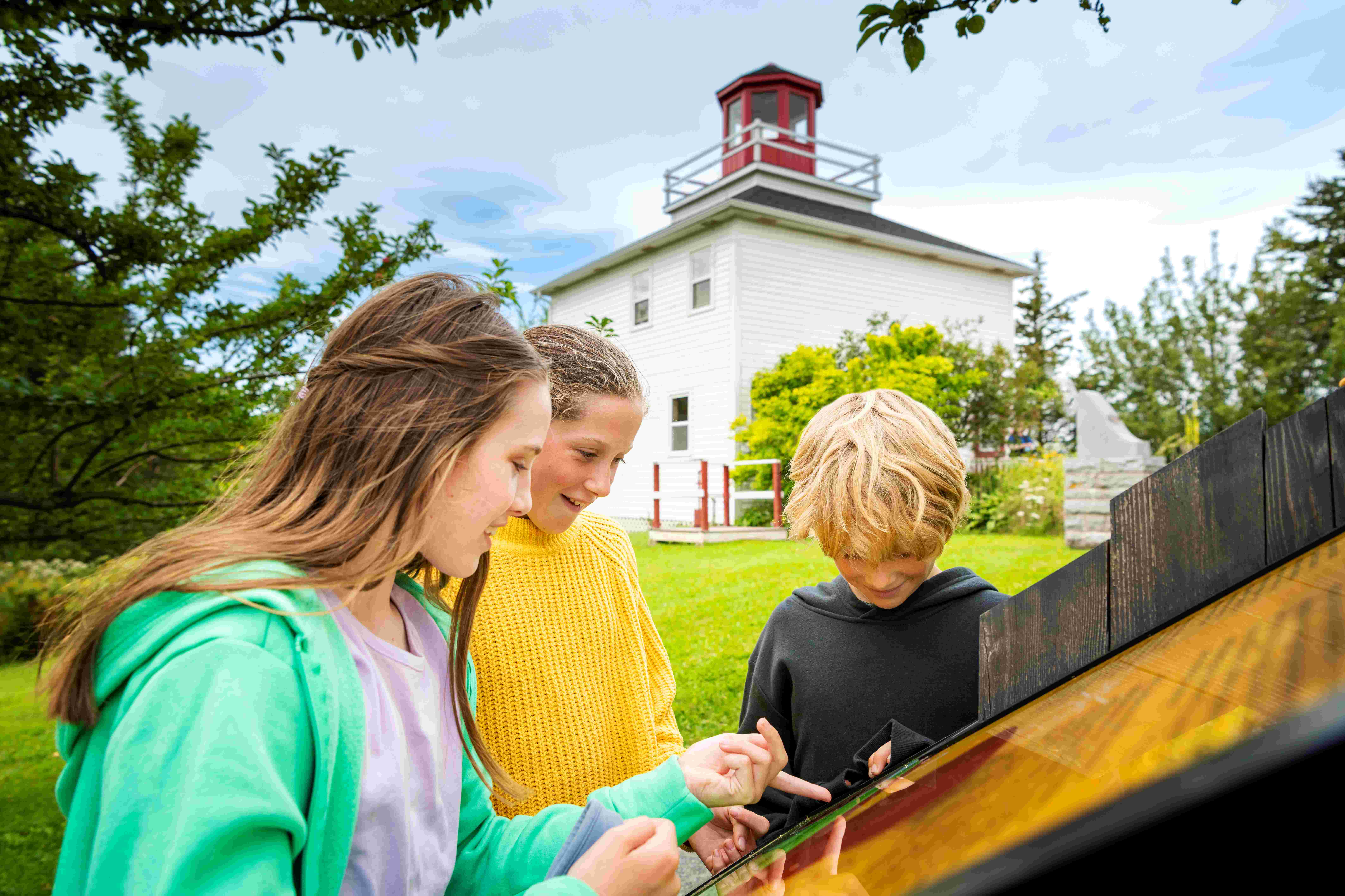 Three children read an interpretive panel while the Burntcoat Head Park lighthouse stands in the background