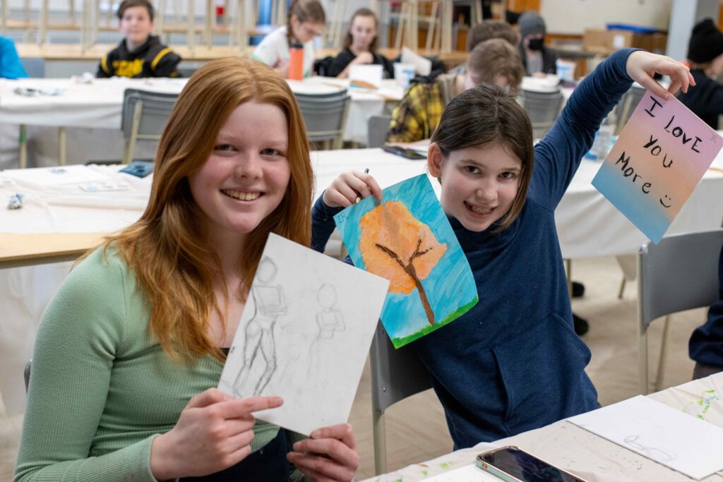 Two girls smile and hold up artwork they have made