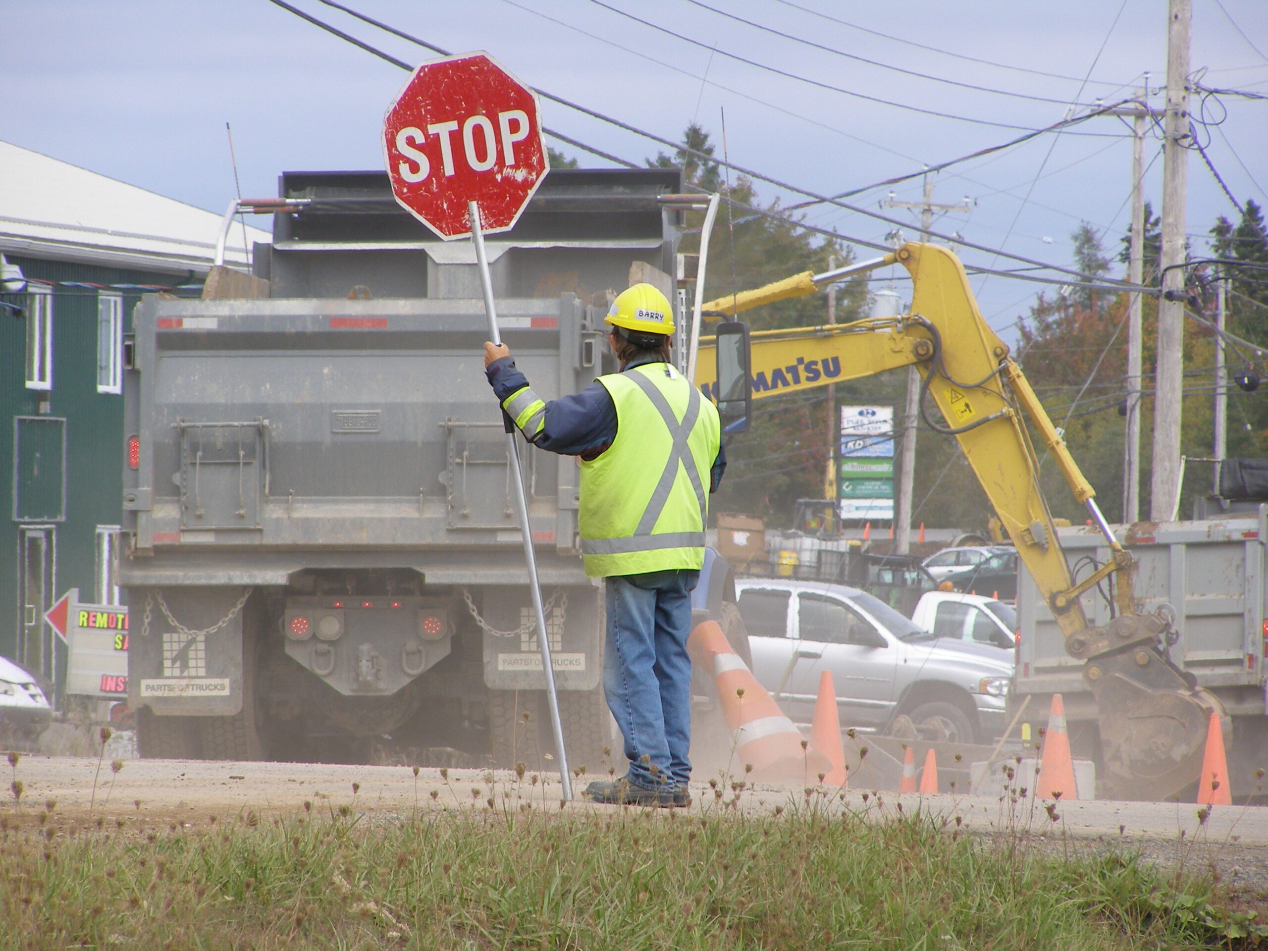 Construction flagger holds a stop sign while a dump truck passes in the background
