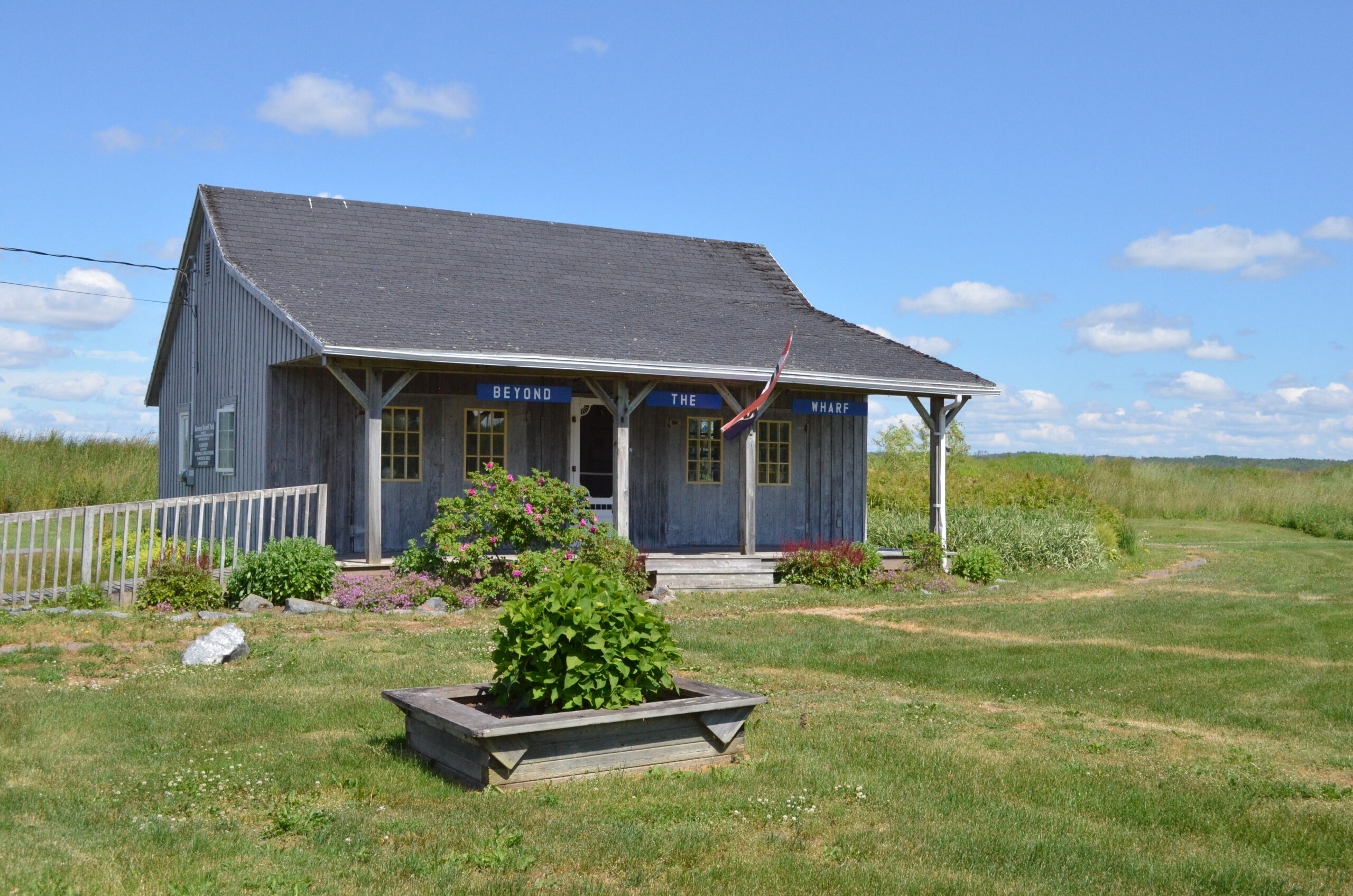 A rustic blue building with a covered porch and decorative shrubs.