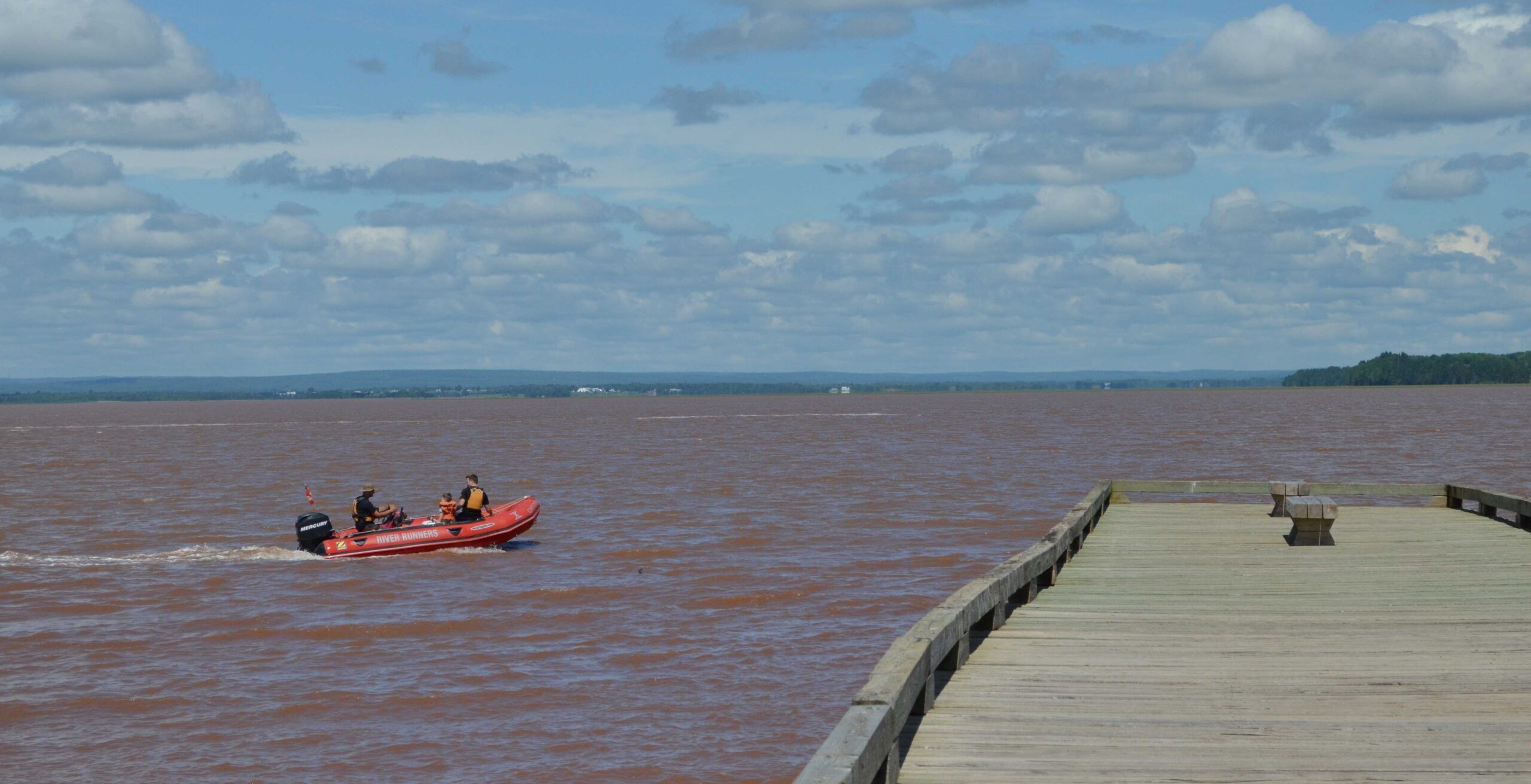 A red zodiac boat cruising across the water towards the end of a long wooden wharf
