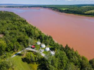 Aerial view of four white geodesic camping domes looking out over high tide on the Shubenacadie River