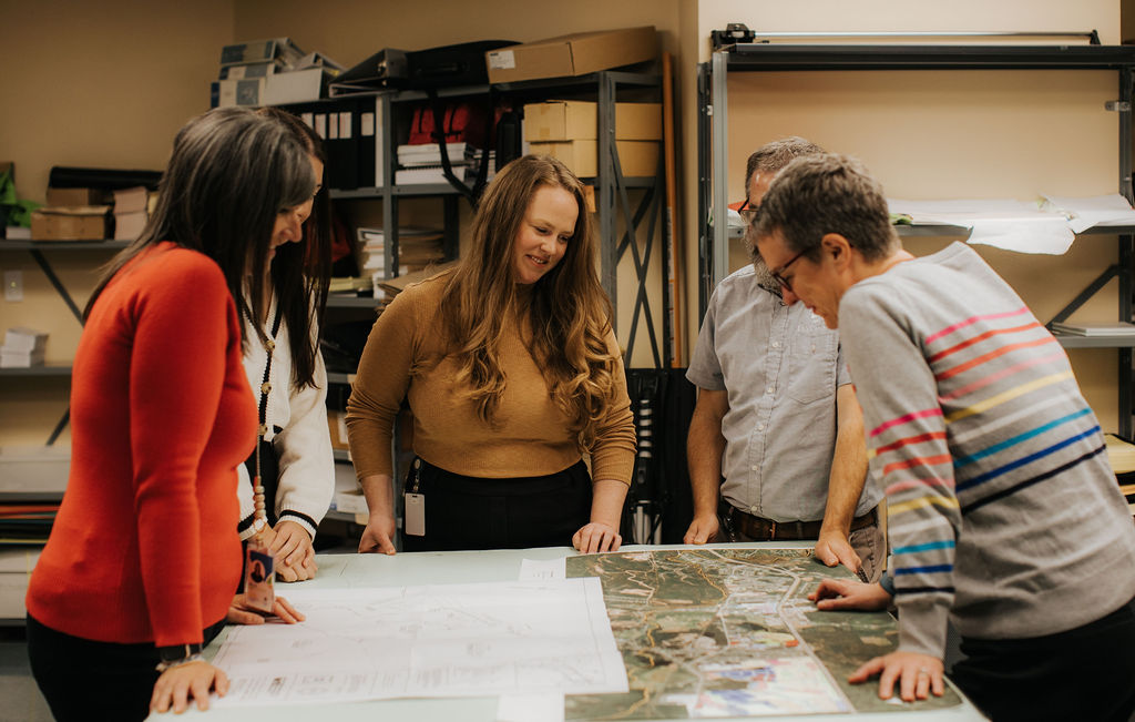 group of people stand around a table talking and looking at a community map