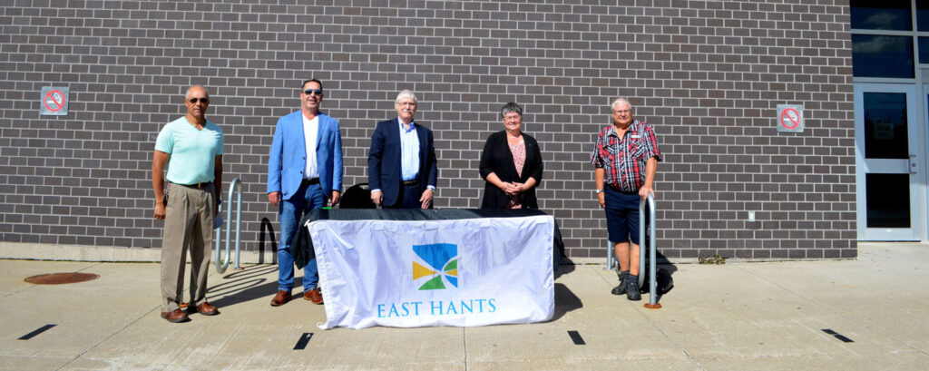 Five people in front of a brick wall, standing behind a table with a white tablecloth bearing the East Hants logo