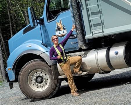 A woman stands holding the door of a large blue dump truck