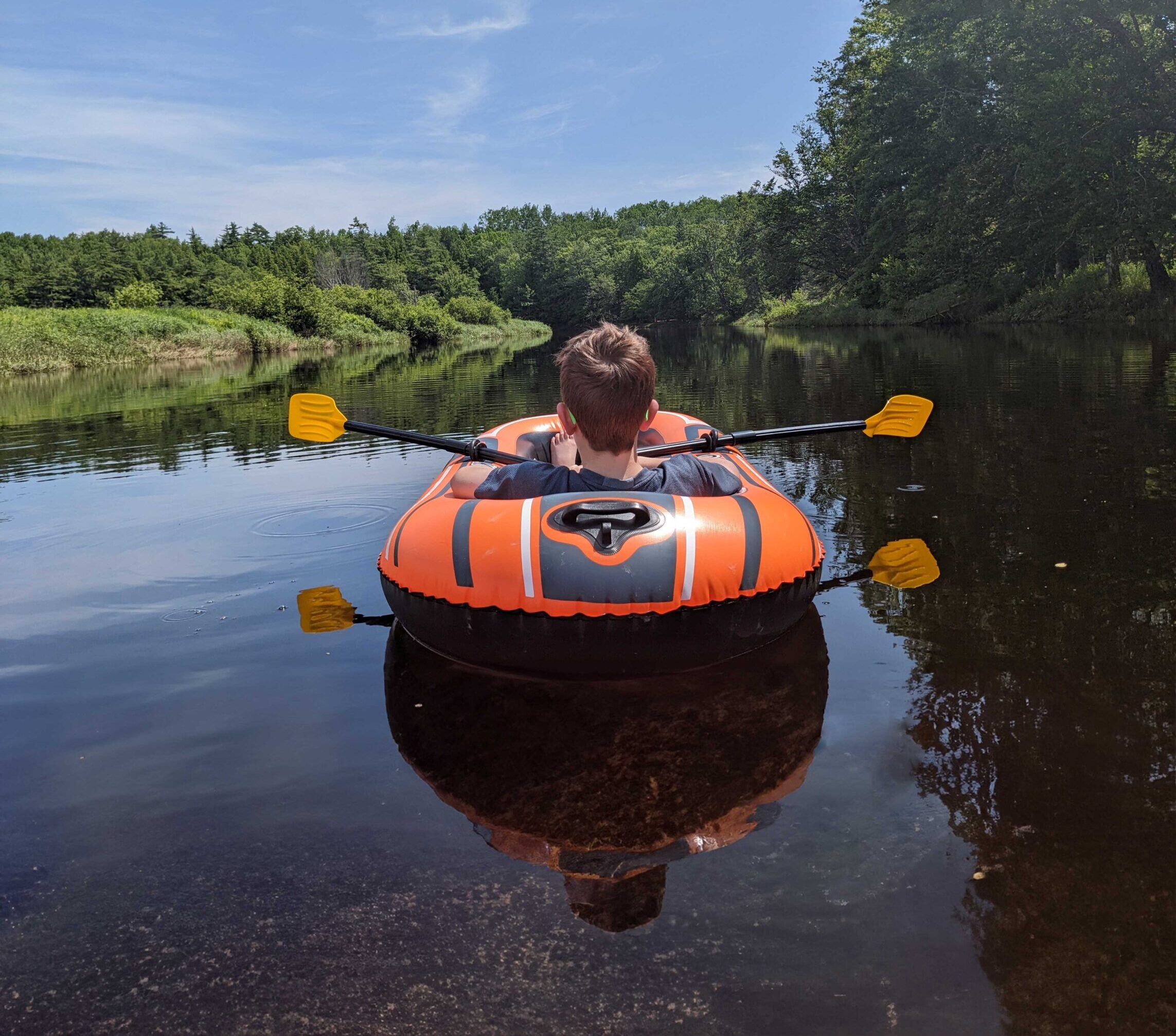 A child in an inflatable boat drifts down a calm river